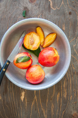 Close up of whole and slices of fresh ripe honeyed nectarines (peaches) with leaves and water drops in a vintage bowl on a wooden board. Summer fruits concept. Rustic style.