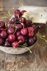 Sweet fresh ripe burgundy cherries with water drops in a bowl on a wooden background. Close up and copy space.
