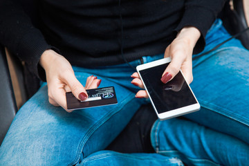 female hand holding plastic credit card and using smartphone