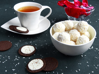 Red terry tulips on notes and round sweets with almonds and coconut in a glass bowl on flower petals on a dark horizontal background.The concept of the feast