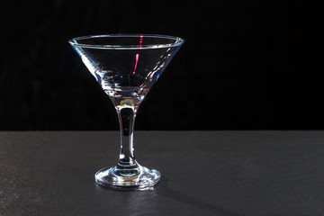 empty glass on a high leg stands on a black granite surface