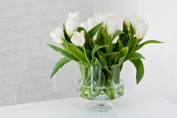 Białe tulipany w szklanym przeźroczystym wazonie na białym tle.