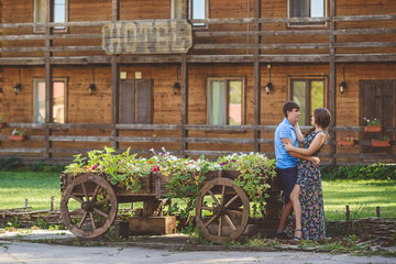 Romantic young couple hugging each other near a decorative wooden carts with flowers, on a background of rustic style.