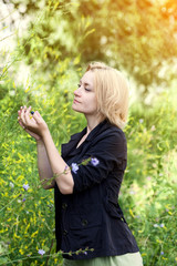 young blonde girl in nature, is about trees and bushes, a hand holding a branch, summer day in the Park outdoors