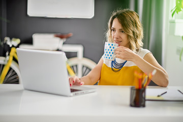 Beautiful Caucasian woman using laptop computer while drinking coffee and sitting personal workspace