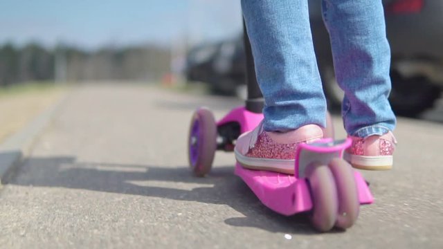 A child is riding a scooter on a sunny day. Slow motion