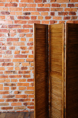 Wooden brown folding screen on a brick background