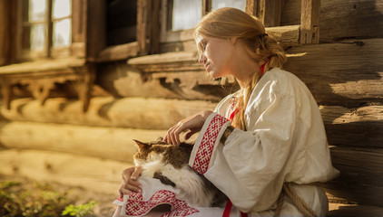 russian woman with a cat near old wooden house in a village