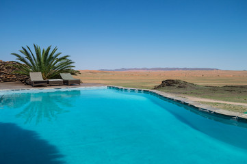 Fototapeta na wymiar Pool with Palm and Sun Beds in a Desert Landscape near Solitaire, Namibia