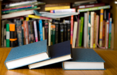 Three books on wooden desk in front of the bookshelf