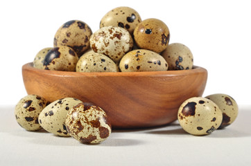 Quail eggs in a wooden bowl on a white