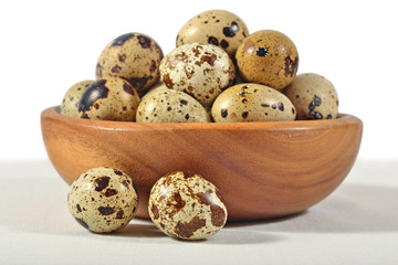 Quail eggs in a wooden bowl on a white