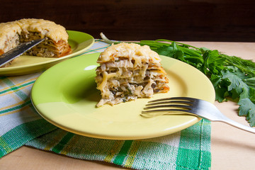 Piece of pancakes pie with mushrooms and chicken meat on green plate and metal fork. Traditional meal for Maslenitsa - Russian pancake week..