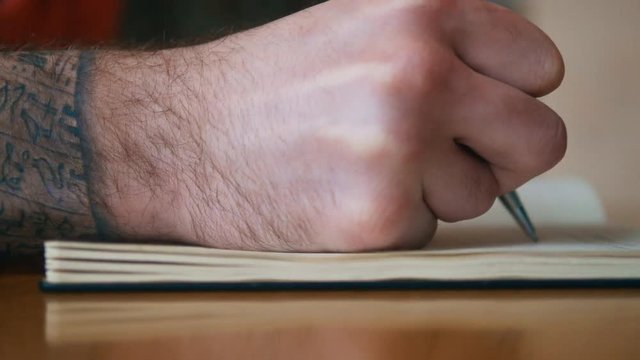 Close up male hand with tattoo writing on a notebook