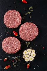 Fresh raw meat burger cutlet on the black slate board with herbs and spices for background.  top view ..