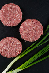Fresh raw meat burger  cutlet on the black slate board with green onion