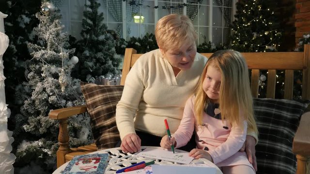 Happy Grandma Teaches Little Girl to Draw Christmas Evening Holiday Interior of the Studio Lights Are Sparkilng in Cosy Room Vacation With Granny Childhood