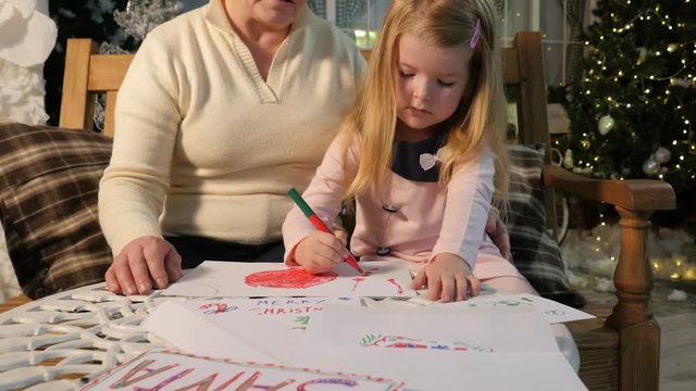 Close View of Family Drawing Together New Year Interior of the Studio Grandma and Little Girl Lights Are Sparkilng on a Background Evening in Cosy Room
