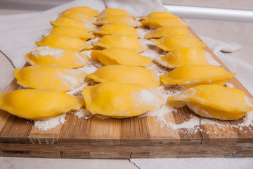 Ready for boiling vareniki, dumplings, pierogi on wooden cutting board with flour and wooden...