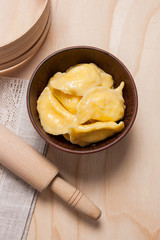 Fresh boiled varenyky or dumpling with cottage cheese or curd in clay bowl on wooden background.