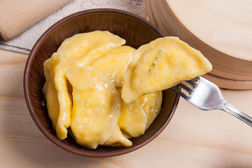 Close up view of boiled varenyky or dumpling with cottage cheese or curd on metal fork. Fresh boiled homemade ukrainian dumplings in clay bowl on wooden background..