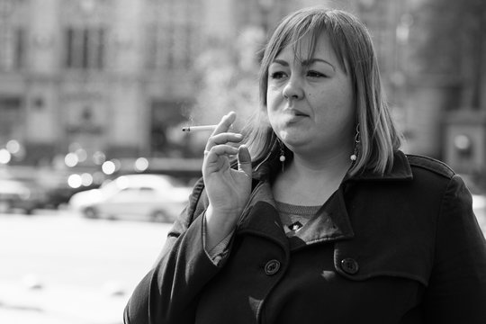 A young large woman with red short hair size plus a size in her coat walks in the city and smokes cigarettes thinking about life and her problems