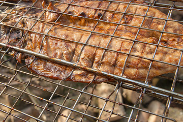Close up view of fresh fish with sauce cooked on an open flame grill..