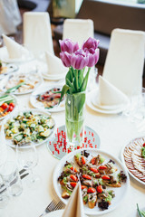 Violet tulips stand in a glass vase on dinner table