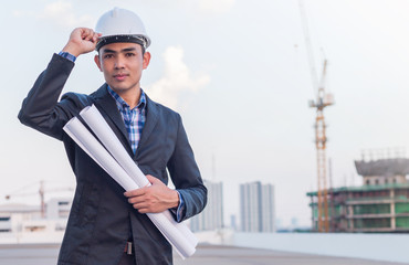 The architect wear white safety helmet and hold the blueprint with commitment to success at construction site with crane background