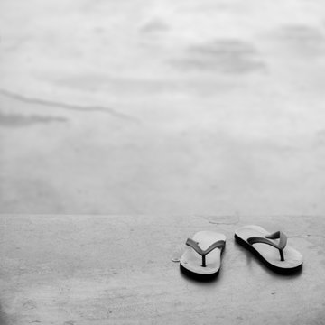 BLACK AND WHITE PHOTO OF PAIR OF FLIP FLOPS ON CONCRETE GROUND
