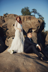 Groom sits beneath bride's feet on the rocks