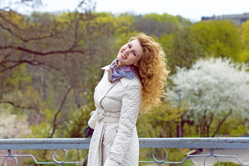Beautiful nice young blonde girl in white coat in romantic style walking around city park laughing and smiling experiencing positive emotions and loving life