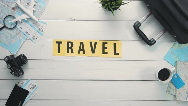 Top view time lapse hands laying on white desk word "TRAVEL" decorated with travel items