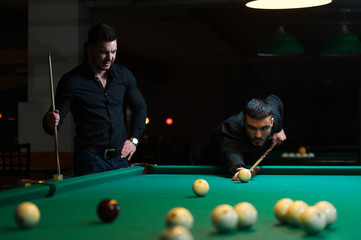 Fototapeta premium Two male friends playing billiard game in club