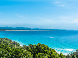 The beautiful view in sunny day with clear blue sky  on the bright blue ocean and on the mountains and on the beach with surfers from Byron Bay Lighthouse, Australia
