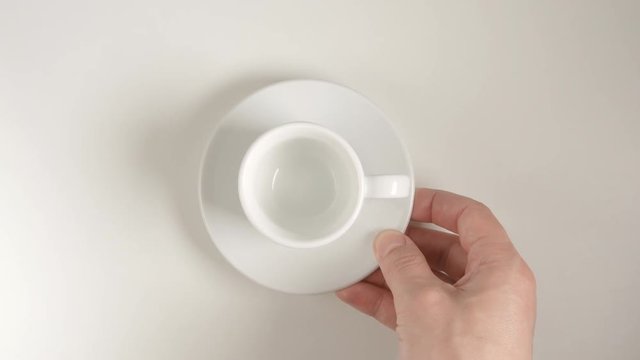 TOP VIEW: Human hand puts a white coffee cup on a white table