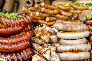 assorted sausages grilled on skewers on a large plate, tomatoes on the grill. Street festival food.