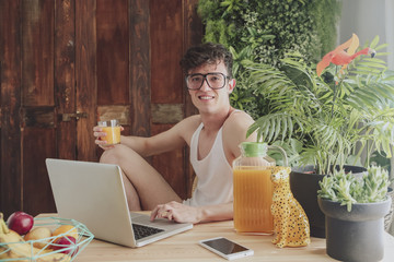 Young man using laptop and drinking orange juice at home