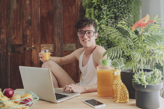 Young man using laptop and drinking orange juice at home