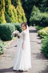 The beautiful bride keeps a bouquet and walking along park