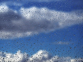 Water drops at the window glass at the blue sky with the rainy clouds background