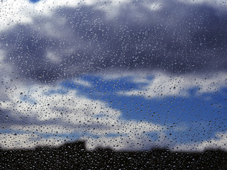 Water drops at the window glass at the blue sky with the dark rainy clouds background