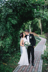 Groom holds his hand on bride's curvy back while they pose on pavement path