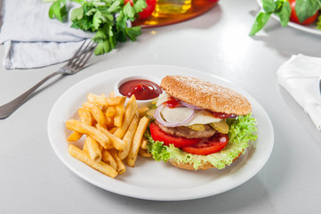 Tasty burger set - meat burger, french fries and sause on the white round plate on the served table with fresh ingridients. Close- up. selective focus. Unhealthy food concept
