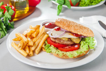 Tasty burger set - meat burger, french fries and sause on the white round plate on the served table with fresh ingridients. Close- up. selective focus. Unhealthy food concept