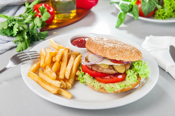 Tasty burger set - meat burger, french fries and sause on the white round plate on the served table with fresh ingridients. Close- up. selective focus. Unhealthy food concept