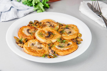 Potato pancakes with mushrooms on the white plate on the table with different bright ingredients, restaurant menu, Selective focus