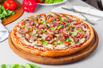 Selective focus close up Delicious Meat Pizza with bacon and sausages on the wooden board on the kitchen table with different bright ingredients