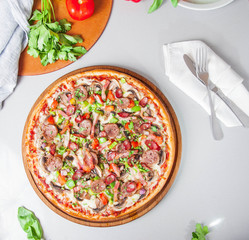 Selective focus close up Delicious Meat Pizza with bacon and sausages on the wooden board on the kitchen table with different bright ingredients