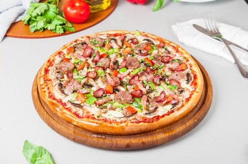 Selective focus close up Delicious Meat Pizza with bacon and sausages on the wooden board on the kitchen table with different bright ingredients